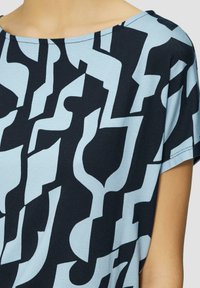 Korte mouw top met een zwart en lichtblauw abstract patroon, ronde hals, zachte stof en een ontspannen pasvorm.