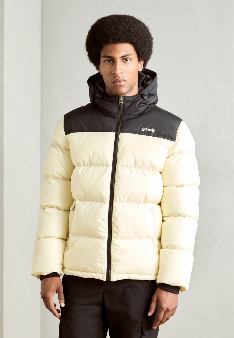 Giacca a vento in giallo pallido e nero. Design trapuntato, colletto alto, cappuccio regolabile e chiusura con zip. Il tessuto è liscio e leggero.