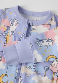 Vaaleanlila haalari, jossa on yksisarvisia, pilviä ja karkkikuvioita. Valmistettu pehmeästä kankaasta, etuvetoketjulla ja ribbaustimilla. 