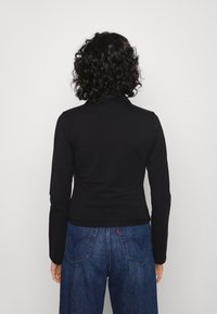 Black long-sleeve top with a high neckline, fitted design, and soft texture, paired with blue high-waisted denim jeans featuring back pockets.