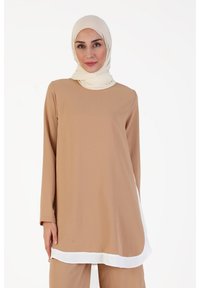 Tunique beige à manches longues et ourlet incurvé blanc. Tissu doux et lisse avec une texture minimale. Accompagnée d'un hijab crème.