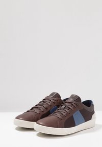 Para brązowo-granatowych sneakersów sznurowanych z białymi podeszwami, oznaczonych marką "Geox", pokazanych pod lekkim kątem na białej powierzchni.