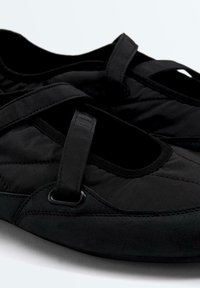 Chaussures Mary Jane noires en tissu matelassé, bride avant réglable, bout arrondi et semelle basse, présentées en gros plan.