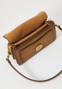 Brown leather handbag with a smooth texture, features a gold toggle clasp, zippered compartment, and a detachable shoulder strap.