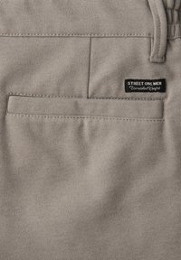 Poche arrière d'un pantalon beige pour homme avec une étiquette noire cousue au-dessus de la poche portant l'inscription « STREET ONE MEN Confort Inégalé ».
