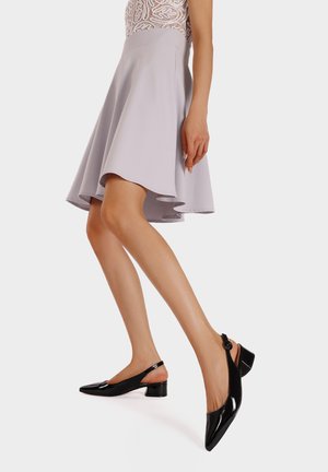 Scarpe slingback in vernice nera con punta appuntita e tacco basso a blocco, caratterizzate da un sottile taglio e un accento a forma di pulsante rotondo.