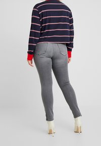 Granatowa bluzka z długimi rękawami w paski z czerwonymi akcentami, zestawiona z dopasowanymi szarymi dżinsami i kremowymi kozakiem na obcasie, ukazująca prosty design i dopasowany krój.