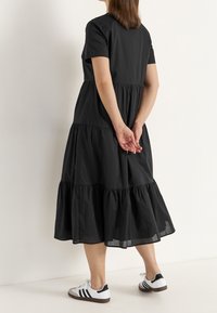 Schwarzes gestuftes Kleid mit kurzen Ärmeln, mit lockerem Schnitt und gesammeltem Saum, kombiniert mit weißen und schwarzen Sneakern.