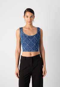 Top de denim cortado con un patrón de diamantes, que cuenta con tirantes anchos y un escote redondo. Lleva puesto con pantalones negros.