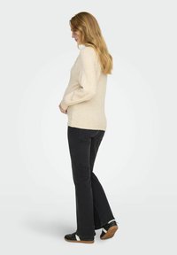 Maglione beige chiaro con polsini a coste, abbinato a jeans neri e scarpe nere con accenti bianchi. Texture morbida e design casual.