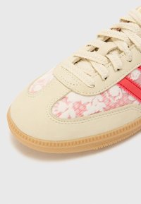 Sneaker beige con pannelli in tessuto floreale rosa e bianco, una striscia di accento rossa e suola in gomma testurizzata. Design con lacci.