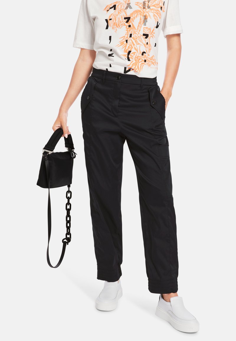 Schwarze Cargo-Hosen aus leichtem Material, mit Fronttaschen, Knopfverschlüssen und schmal zulaufenden Beinen, kombiniert mit einem weißen Grafik-T-Shirt und Turnschuhen.