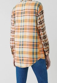 Camicia a quadri con una combinazione di toni arancioni, gialli e blu. Maniche lunghe con polsini a bottone e orlo curvo. Tessuto morbido.