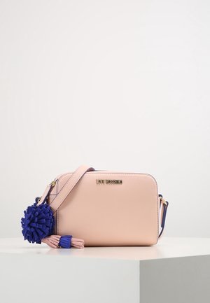 Sac bandoulière Love Moschino rose clair avec logo doré et accessoire pompon à franges bleu et rose sur une surface blanche.