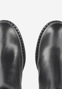 Bottines en cuir noir à finition lisse, avec un bout arrondi et des détails texturés sur les côtés. Dotées d'une semelle noire robuste et rainurée.