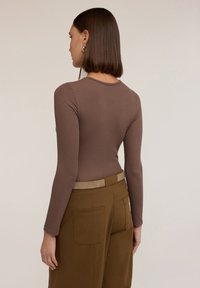 Langsleeve, geribbelde bruine top met een ronde hals, gecombineerd met hoge bruine broeken met een lichtbruine riem en zakken.
