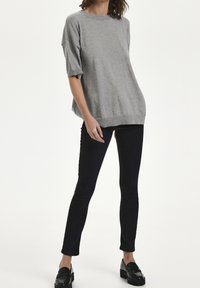 Grå, oversize strikket sweater med korte ærmer, rund halsudskæring og ribbet kant, parret med sorte slim-fit jeans og sorte loafers.