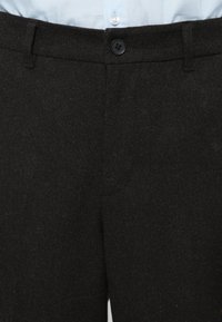 Mustad villased püksid, millel on sile tekstuur, nööpkinnitus ja standardne vöökoht. Muster ega aksessuaare pole nähtaval.