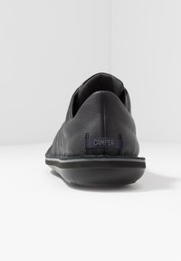 Black leather slip-on shoe with rounded toe, low profile, and a textured finish. Features a visible Camper logo in navy at the heel.