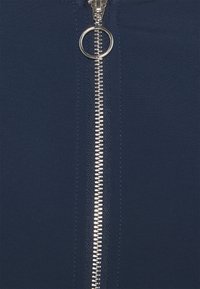 Giaccone blu navy con zip in metallo argentato e una linguetta circolare, caratterizzato da una superficie liscia su tutta la stoffa.