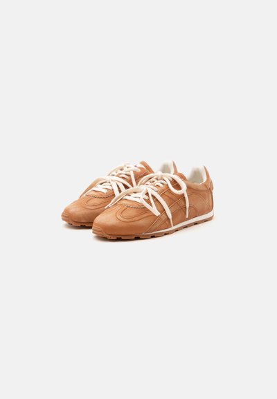 Paire de baskets en cuir marron clair avec lacets blancs et semelles en caoutchouc blanc sur un fond clair uni.