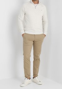 Felpa grigia chiaro con zip e collo alto, pantaloni chino beige e scarpe da ginnastica bianche. Il tessuto sembra morbido con una texture sottile.