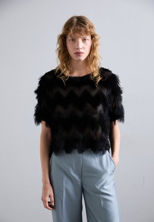 Svart kortermet topp med et teksturert chevronmønster, med frynser langs kantene. Kombinert med lys blå, skræddersydde vide bukser.