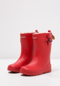 Røde vandtætte gummistøvler med en tekstureret overflade, rund tå og et logo nær toppen. Har en spænde og en bageste hævetap.