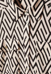 Chemise à motifs noir et blanc avec un design en zigzag, devant à boutons, col pointu et deux poches poitrine, en tissu léger.