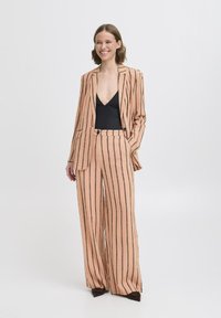 Blush-pink Gestreifter Anzug mit weiten Hosen und einem figurbetonten schwarzen Bodysuit. Die Jacke hat einen Reverskragen und zwei Knöpfe.