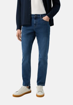 Dunkelblaue Jeans im geraden Schnitt mit einem klassischen Fünf-Taschen-Design. Kombiniert mit weißen Sneakern und einer marineblauen Strickjacke.