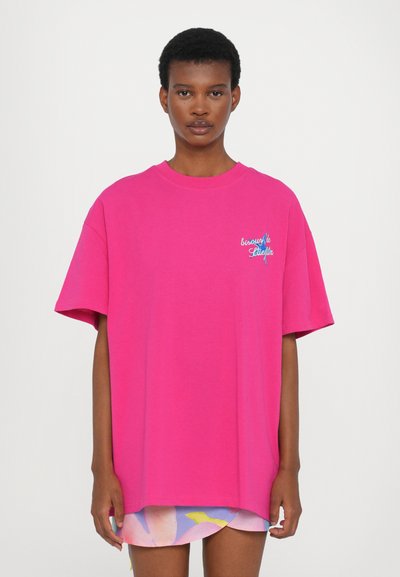 T-shirt surdimensionné rose en coton. Présente un col rond et des manches courtes. Comprend un texte brodé en bleu sur la zone de la poitrine.