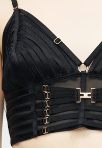 Μαύρο σουτιέν bralette με διάφανα δίχτυα στα πλαϊνά, πλισέ κύπελλα, ρυθμιζόμενους ιμάντες και πολλαπλούς γάντζους σε χρυσό τόνο μπροστά και στα πλάγια.