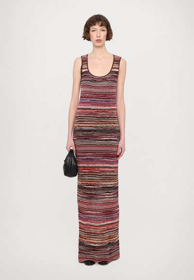 Knit sleeveless maxi dress featuring horizontal stripes in red, pink, and brown hues. The fabric has a textured finish. Paired with a black bag.
