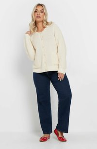 Krämfärgad stickad cardigan med ett strukturerat mönster, rund halsringning och knappar framtill. I kombination med mörka jeans och röda ballerina-skor.