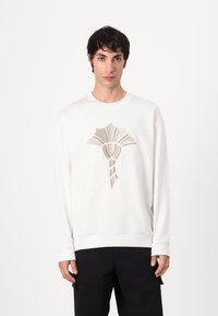 Sudadera blanca con un patrón decorativo tejido en color beige en el centro. Cuello redondeado y mangas largas con puños acanalados.