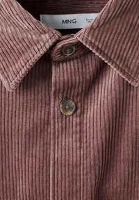 Manchester-skjorta i dammig rosafärg med en vid krage, som har en vertikal räfflad textur och två runda knappar framtill.