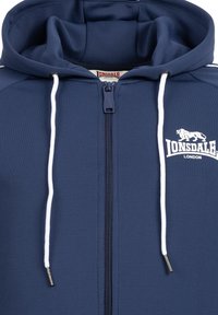 Marineblå zip-hoodie med hvide snore, prydet med et logo og kontrasterende striber. Fremstillet af glat, struktureret stof med en afslappet pasform.