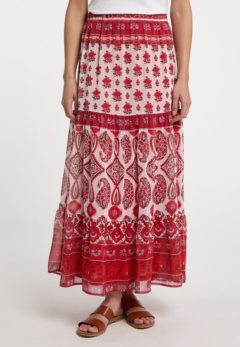 Maxi rok van doorzichtig materiaal met een bloemenprint in rood en roze, voorzien van gelaagde ruches en een comfortabele elastische taille. Bruine instapsandalen eronder.