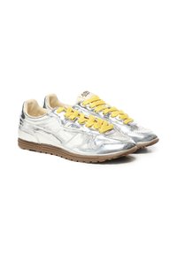 Zapatillas metálicas plateadas con cordones amarillos, textura de cuero suave y suela de goma marrón con detalle de logo embellecido en el lateral.