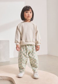 Beiger Pullover mit gerippten Bündchen, kombiniert mit grün-pink karierten Hosen. Weiße Turnschuhe vervollständigen das Outfit.