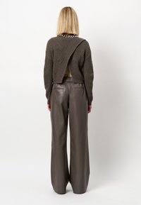 Donkergrijze gebreide trui met getextureerde golven en open achterkant, gedragen over een high-waisted brede bruine leren broek.