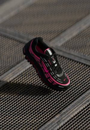 Schwarzer Sportschuh mit pinken Akzenten, ausgestattet mit einer strukturierten Oberfläche, rundem Zehenbereich und einer gepolsterten Sohle. Schnürsenkel und Branding-Details sind sichtbar.