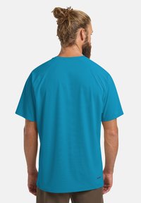 T-shirt attivo a maniche corte di un brillante colore turchese, caratterizzato da una texture liscia e maniche raglan, con un logo nella parte bassa della schiena.