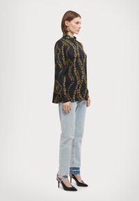 Camisa preta com um padrão de corrente, colarinho abotoado, mangas longas. Usada com jeans azul claro e sapatos de salto agudo pretos.