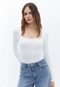 Witte long-sleeve bodysuit met een vierkante halslijn, een gladde textuur, gecombineerd met hooggetailleerde lichtblauwe denim jeans met een klassieke vijfvakdesign.