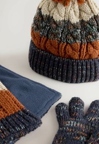 Knit hat in orange, cream, and navy with a pom-pom; fleece scarf in blue; knitted gloves with multi-color accents. Textured and warm.