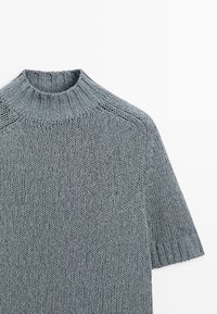 Grå kortærmet strikket sweater med ribstrikket høj krave og ærmer, med en tekstureret, chunky strikket mønster.