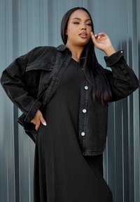 Mustat farkkutakki hopean väristen nappien kanssa, joka on puettu mustan ribbivaatteen päälle. Takki on klassisen ylisuuri ja siinä on kaksi etutaskua.