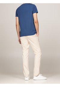 Camisa azul de manga corta, pantalones ligeros beige, zapatillas blancas. Tejido de algodón, corte relajado, con un diseño minimalista y sin patrones ni herrajes visibles.